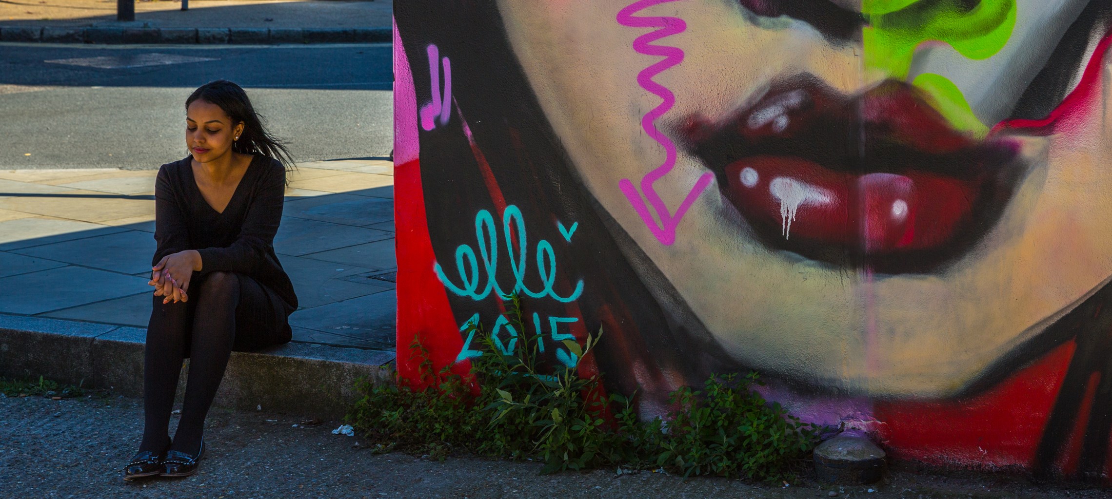 Girl sat on pavement next to graffiti wall