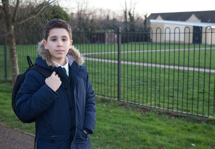 teenage boy standing in front of a fence with a backpack