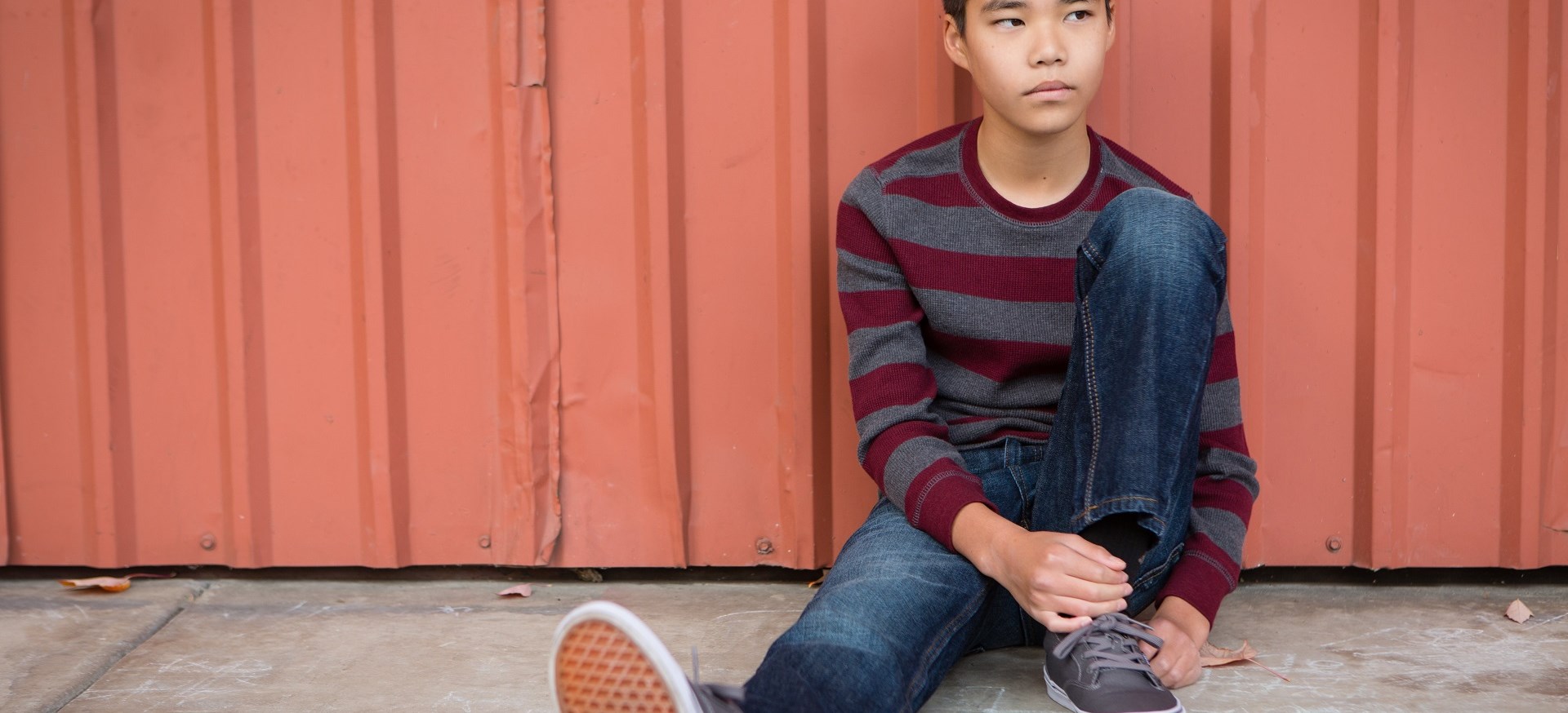 teenage boy sitting leaning against a wall