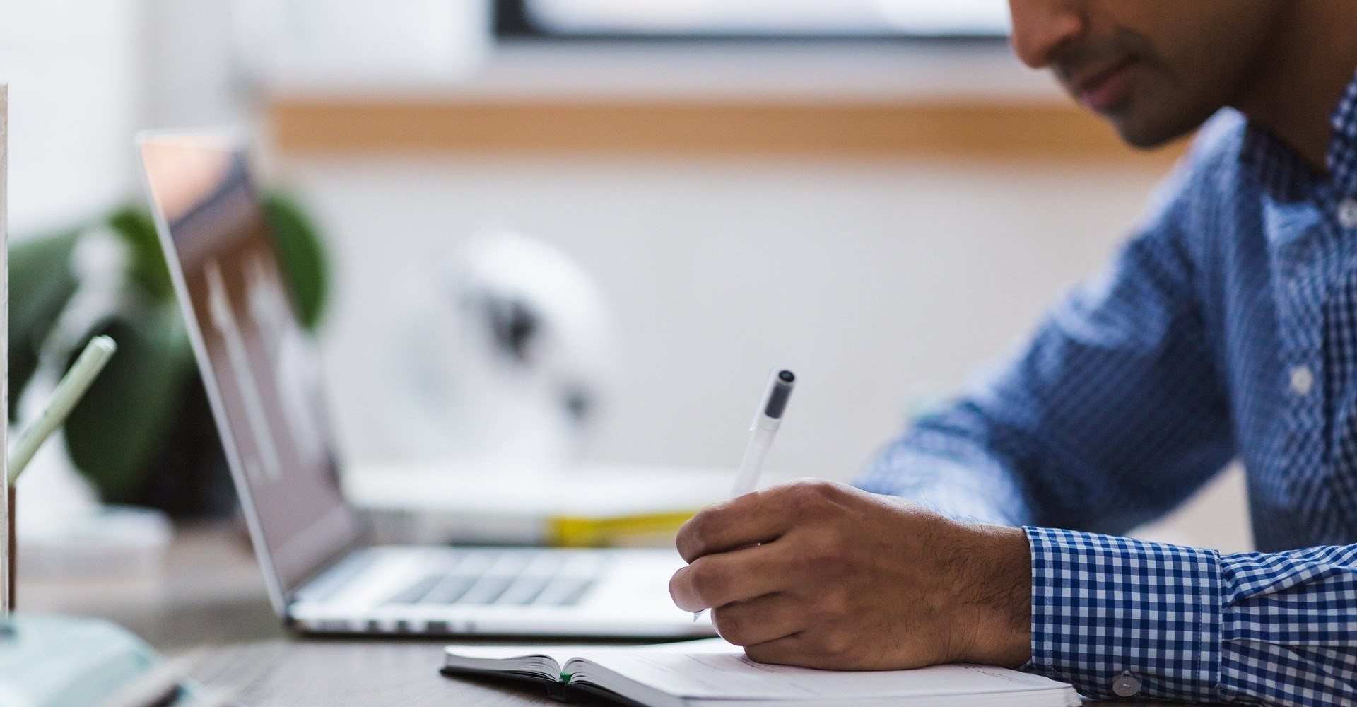 man holding a pen looking at a laptop