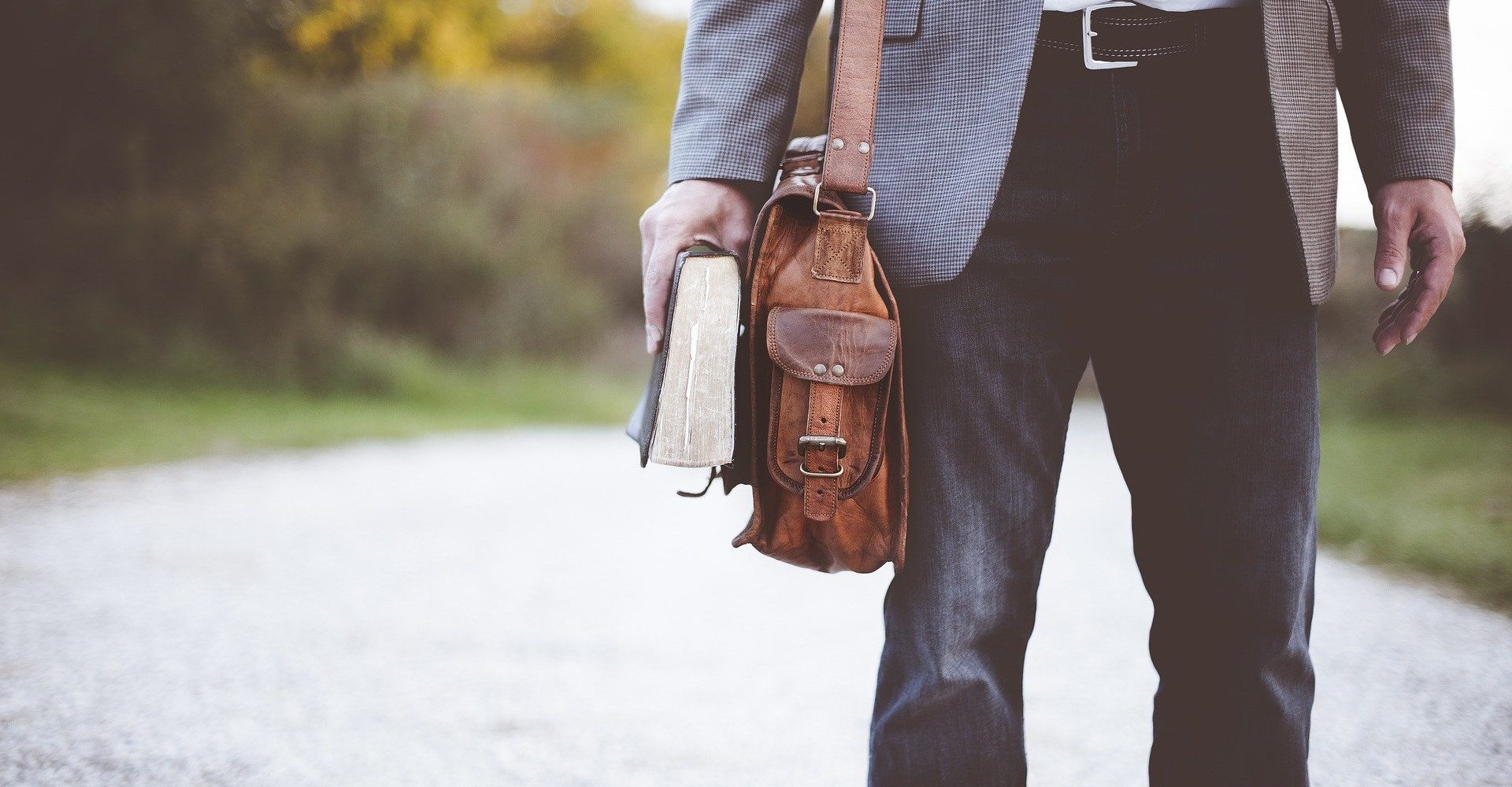 man walking with a bag on his shoulder, carrying a book