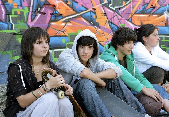 four teenagers sitting on the floor with a skateboard and basketball