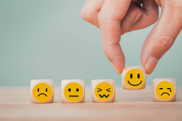 close up of dice with different emoji faces, with fingers picking up the happy face