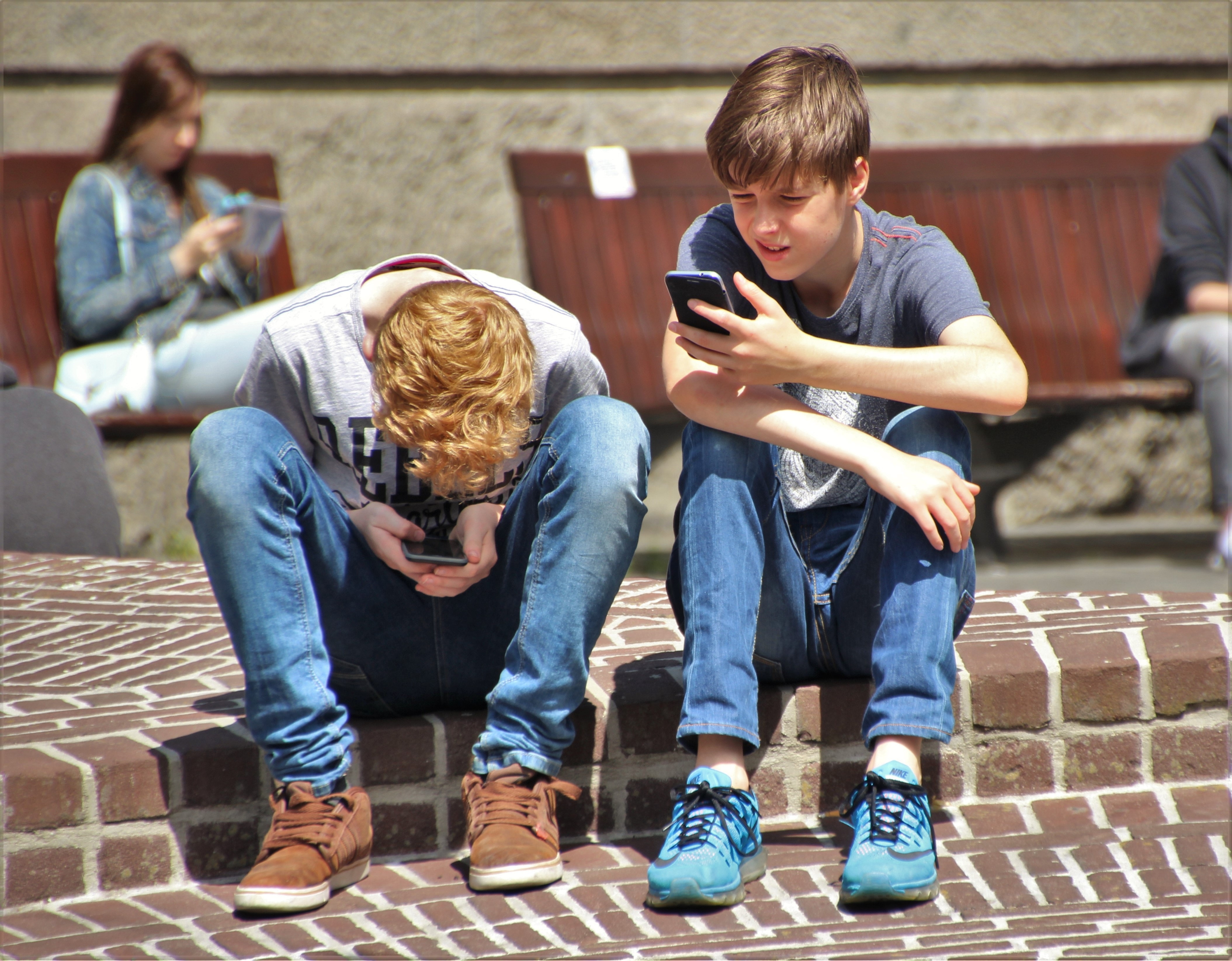 boys sitting on low brick wall outside on their phones