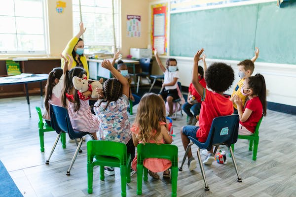 children and teacher sitting in a circle raising hands