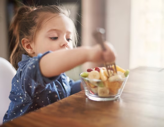 little girl eating bowl of chopped fruit
