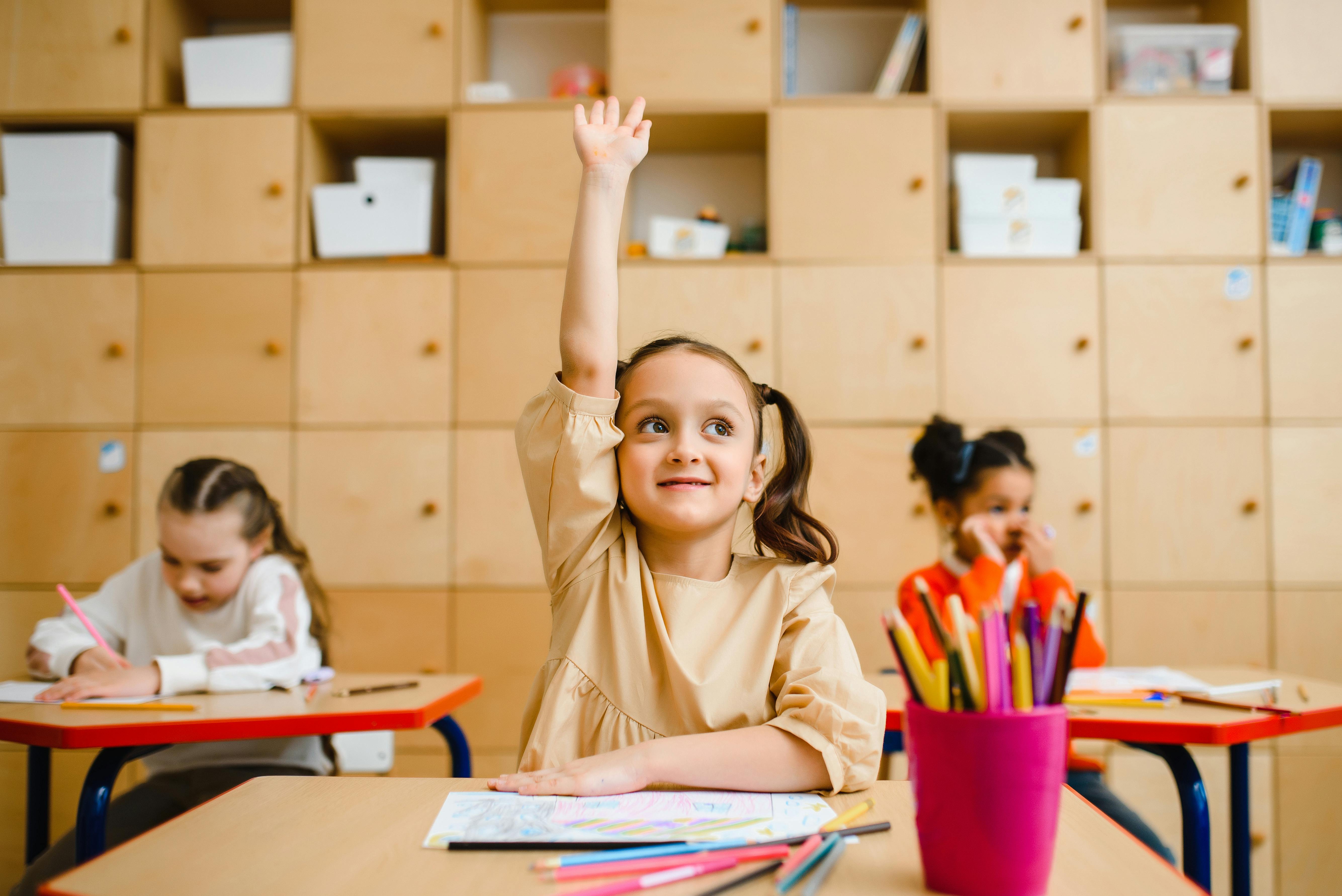 Girl in classroom with her hand raised.