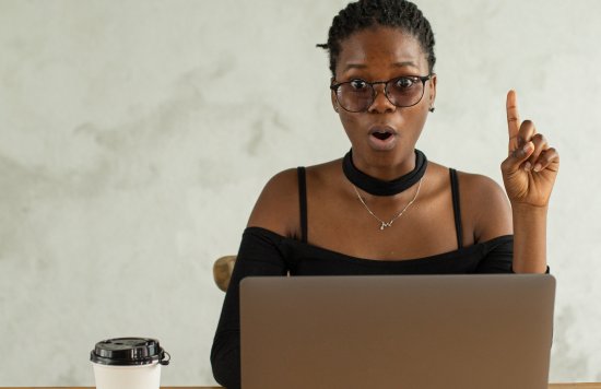 Black female with finger pointing in the air looking surprised at laptop computer with takeaway coffee beside her