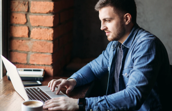 Man sat at desk with laptop and coffee.