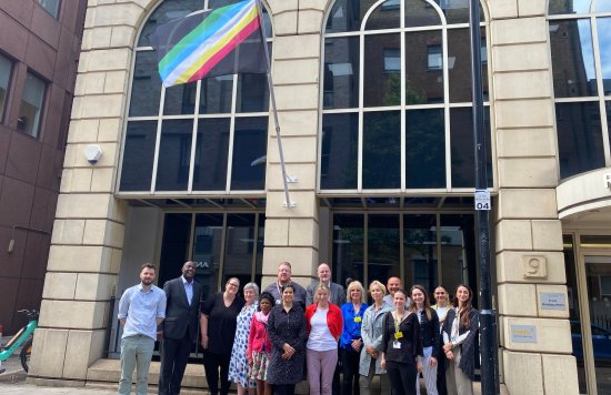 Staff members outside Trust HQ underneath the Disability Pride flag.
