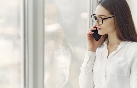 Stock image of a woman on the phone standing next to a window.