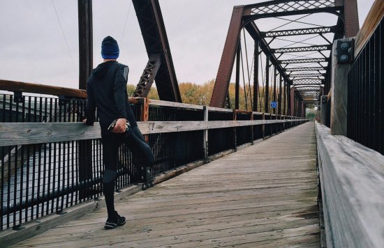 Runner doing leg stretches on a bridge