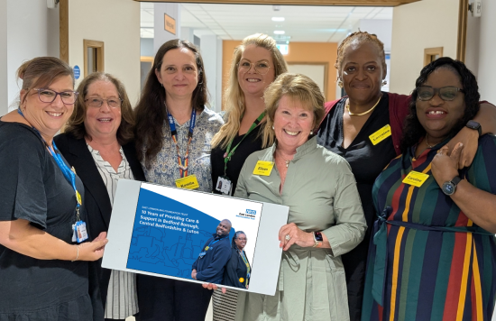 Chair Eileen Taylor and CEO Lorraine Sunduza joined by five ELFT colleagues and holding a copy of the anniversary document