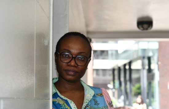Black female in floral dress leaning against a wall