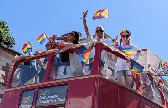 colleagues at london pride on the top of a red double decker bus holding a pride flag in their hands
