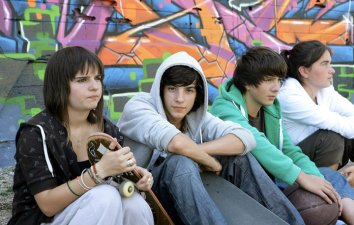 four teenagers sitting on the floor with a skateboard and basketball
