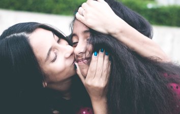Parent kissing her teen daughter's cheek
