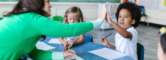 teacher high-fiving a child at a classroom table